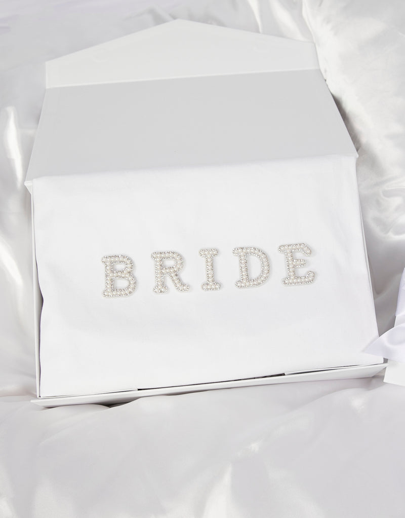 23Dreams Whitehaven Bliss Bridal Box: white tote bag with "bride" pearl and rhinestone patches, 2 petite white gift boxes; one Mini Love hearts Bath Bomb Fizzies; hamptons deluxe candle whitehaven sea salt; ultra soft satin sleep eye mask white; scrunchie soft silky satin white; luxe silky camisole set white; Elegant 18K Gold Plated Letter Pearl Necklace; glamour pearls hair pin set in gold 18 pins; white pearls gold hair pin set luxe glam and white pearled hair clip set in gold timeless elegance.
